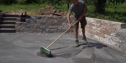 Mitarbeiter kehrt Fugensand auf der Terrasse ein